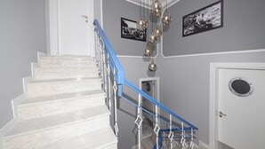 Una escalera con peldaños de mármol blanco y barandillas azules, que conduce a una puerta con un ventanal redondo.