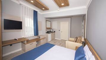 Una habitación de hotel moderna con una cama grande, un escritorio con televisor de pantalla plana, una kitchenette y un baño.