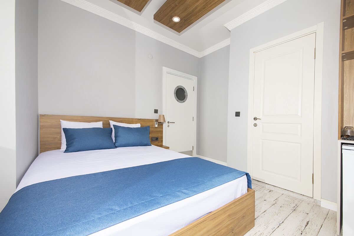 Un dormitorio con cabecera de madera, cama con ropa de cama azul, una puerta blanca y un armario blanco.
