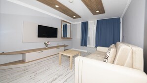 Una sala de estar moderna con un televisor de pantalla plana, vigas de techo de madera, un sofá y una mesita.