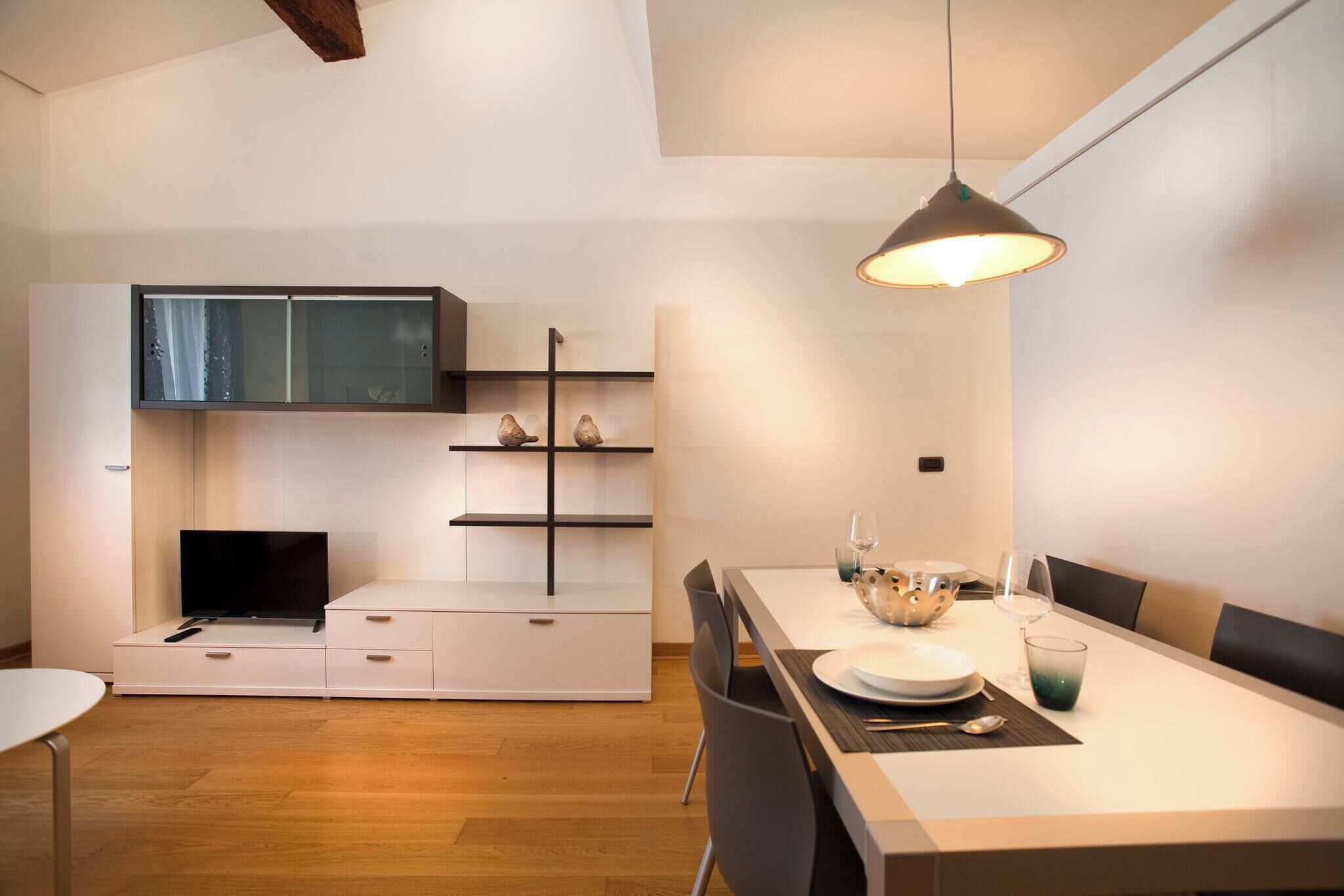 Une cuisine moderne dotée d’un téléviseur encastré, de meubles en bois et d’un coin repas avec une table dressée pour deux personnes.