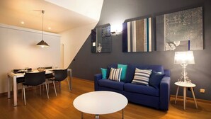 A modern living room with a dining area, a blue sofa, and a white round table.