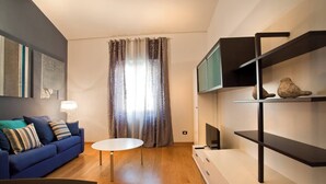 A modern living room with a blue sofa, a white coffee table, and a TV on a black stand.