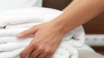 A hand folding a white towel on a bed.