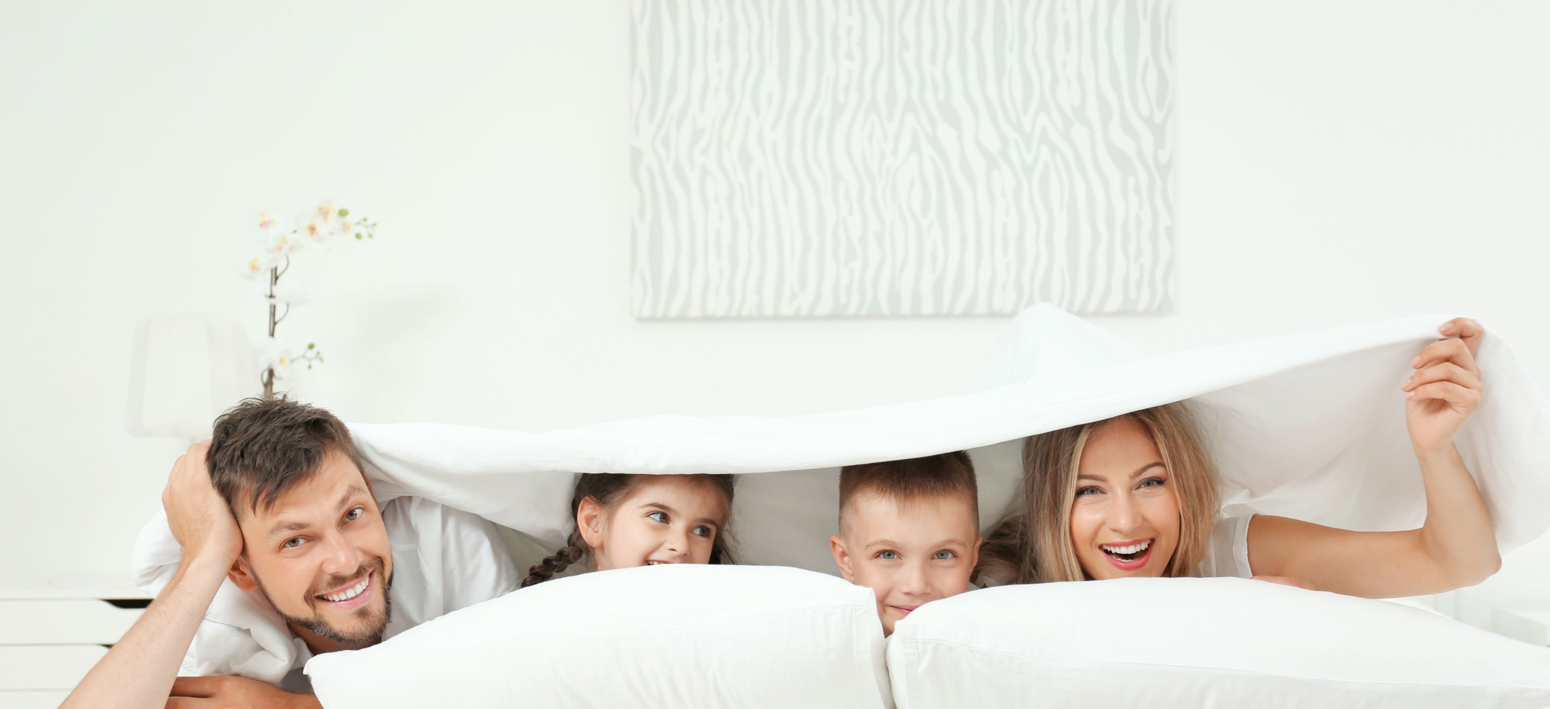 Eine Familie in einem Schlafzimmer mit weißer Bettwäsche und einem Kunstwerk über dem Bett.
