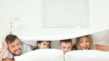 Eine Familie in einem Schlafzimmer mit weißer Bettwäsche und einem Kunstwerk über dem Bett.