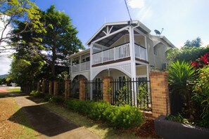 A two-story house with a balcony, surrounded by a brick fence and greenery. - A Touch of the Bahamas on McKenzie MK3 (Cairns)