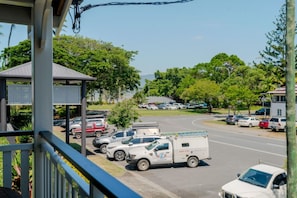 Un espace de stationnement où sont garés plusieurs véhicules, dont un camion utilitaire blanc, et un bâtiment doté d’une passerelle couverte.