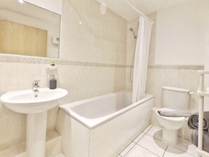 A bathroom with a sink, bathtub, toilet, and shower curtain. - Central Spacious & Stylish Apartment (Oxford)