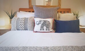 A bed with multiple pillows, including a decorative elephant pillow, and a wooden headboard. - Central Spacious & Stylish Apartment (Oxford)