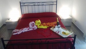 A bed with a red bedspread, a bottle of champagne, and a plate with food on a tray. - Dolcesosta B&B (Pulsano)