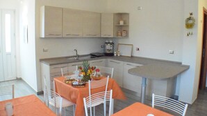 A compact kitchen with white cabinets, a small dining area with orange tablecloths, and a coffee machine. - Dolcesosta B&B (Pulsano)