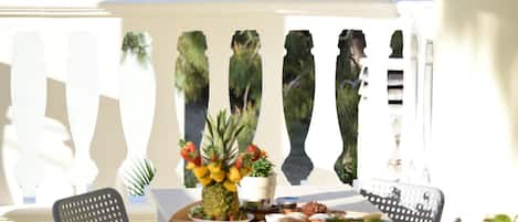 A terrace with a table set for breakfast, including a pineapple centerpiece, a potted plant, and a tray of pastries.