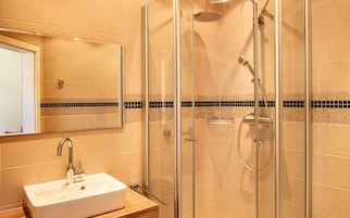 Un baño moderno con ducha de vidrio, lavamanos blanco y salpicadero de azulejos.