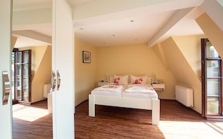 Un dormitorio con cama blanca, suelo de madera y un ventanal grande.