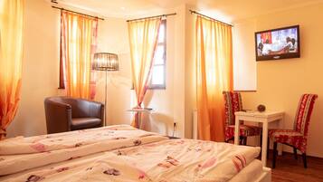 A hotel room with two beds, a desk, a chair, a TV, and curtains.