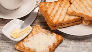 Un plato de pan tostado con mantequilla y una taza de café sobre una mesa de madera.