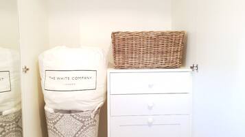 A bedroom with a white wardrobe, a wicker basket on top, and a pillow with "The White Company London" label.