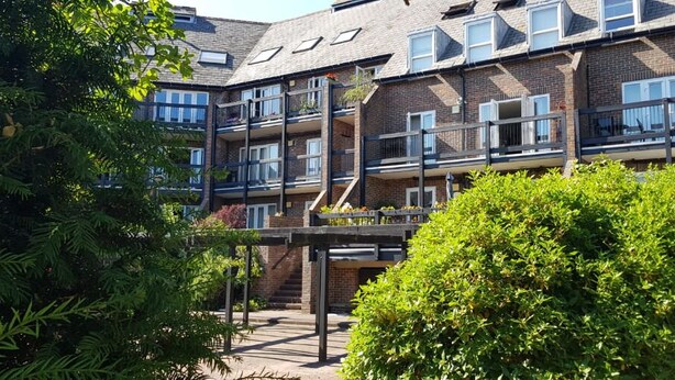 Un edificio de varios pisos de ladrillo con balcones, una escalera y abundante vegetación al frente.