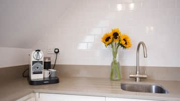 A kitchen with a coffee maker, a vase with sunflowers, and a stainless steel sink.