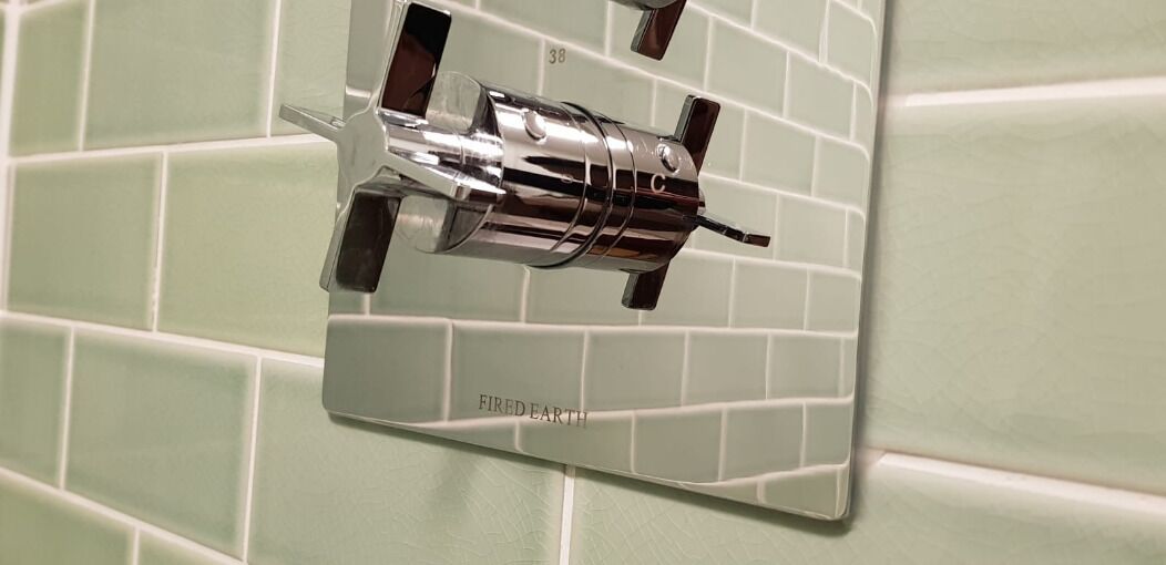 A bathroom with a green tiled wall and a mirror with a chrome faucet.