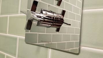 Une salle de bain avec un mur recouvert de carreaux verts et un miroir doté d’un robinet chromé.