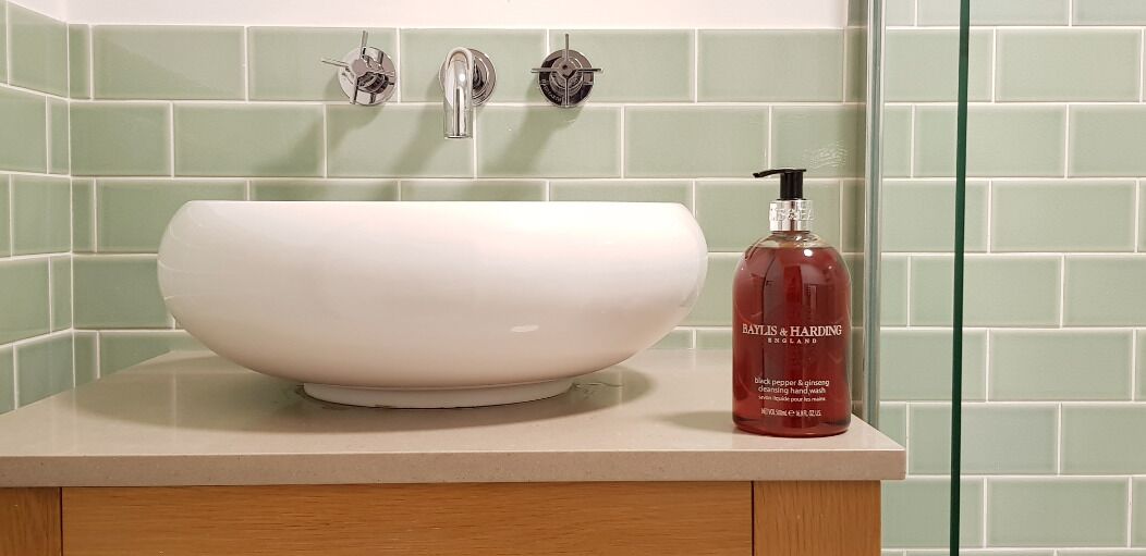 Ein Badezimmer mit einem weißen Waschbecken, einer Baylis & Harding Handseife und einer grün gefliesten Wand.