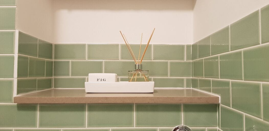 A bathroom with green tiles, a white shelf, and a white box labeled "FIG" with reed diffusers.