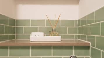 A bathroom with green tiles, a white shelf, and a white box labeled "FIG" with reed diffusers.