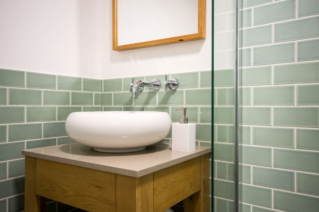 A bathroom with a white sink, wooden cabinet, and green-tiled walls.