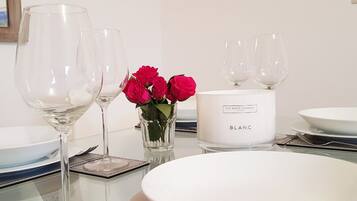 A table set with white plates, clear wine glasses, a white candle labeled "BLANC," and a vase with red roses.