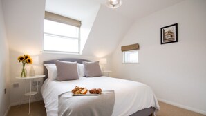 Un dormitorio con cama, mesita de noche, lámpara, ventana y un cuadro en la pared.