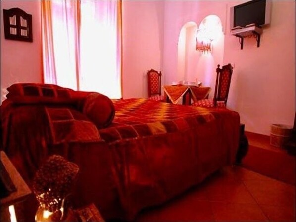 Un dormitorio con una cama grande, un televisor en la pared y una mesita de noche con una lámpara.