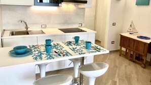 A modern kitchen with white cabinets, a stainless steel sink, and a microwave. There is a small island with stools and a decorative tablecloth. - Holiday House Palau (Palau)