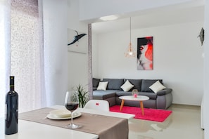 A modern living room with a grey sofa, a small round table, a red rug, and a wine bottle on a table. - Apartments Olujic (Vir)