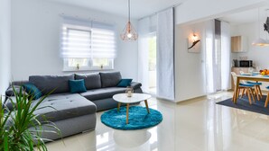 A modern living room with a grey sectional sofa, a round coffee table, and a blue rug. - Apartments Olujic (Vir)