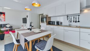 A modern kitchen with white cabinets, a dining area with a table and chairs, and a built-in oven. - Apartments Olujic (Vir)