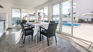 A modern kitchen with a dining area, large windows, and a view of a swimming pool. - Apartments Olujic (Vir)
