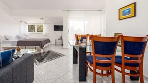 A modern hotel room with a bed, a sofa, a dining table with chairs, a TV, and a window with curtains. - Apartments Pavlak (Vir)