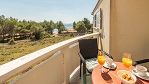 A balcony with a table set for breakfast, overlooking a coastal area with trees and a view of the sea. - Apartments Pavlak (Vir)