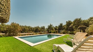 A rectangular swimming pool with a white border, surrounded by a well-maintained lawn and several white lounge chairs. - Apartments Pavlak (Vir)