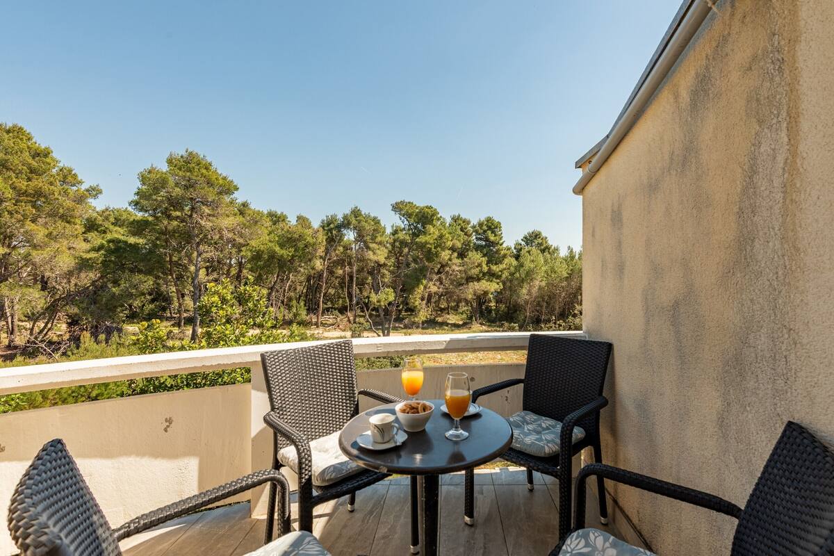 A balcony with wicker chairs, a table with breakfast, and a view of trees.