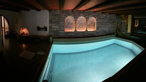 A swimming pool with a stone wall and arched windows, a fireplace, and a mural on the wall. - Villa in the Black Forest with indoor pool (Falkau)