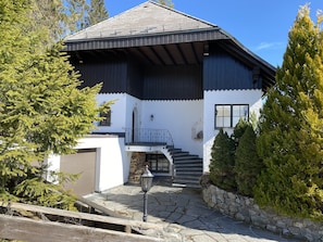 Ein zweigeschossiges Haus mit Natursteinfundament, einer Holztreppe und einem Metallgeländer am Balkon.