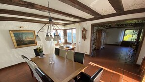 A dining area with a wooden table and chairs, a painting on the wall, and a view of the garden through the window. - Villa in the Black Forest with indoor pool (Falkau)