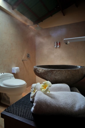 Une salle de bain avec un lavabo en pierre, des toilettes, des serviettes et une fleur.