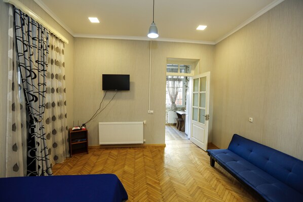 Una habitación con suelo de parqué, un sofá azul, un televisor montado en la pared y un radiador.