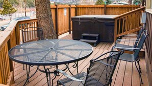 Un terrazza in legno con un tavolo rotondo in metallo e sedie, un barbecue e vista sulle montagne innevate.