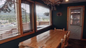 Un tavolo da pranzo in legno con sei sedie, ampie finestre con persiane, una porta con cancello in metallo e un lampadario.