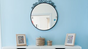 A room with a light blue wall, a white dresser with two framed pictures, a round mirror with a black frame, and a small woven basket. - Casa Vacanza Circe (Sperlonga)